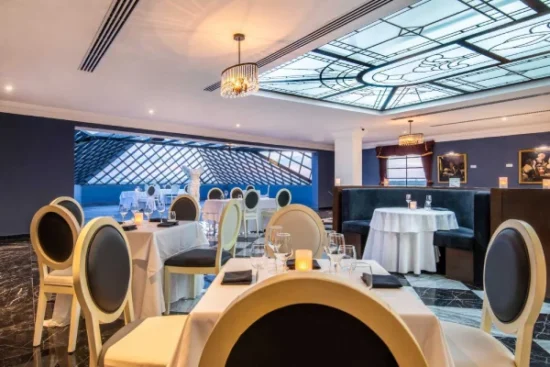 Elegant restaurant interior with dressed tables, modern chairs, and illuminated decorative ceiling.