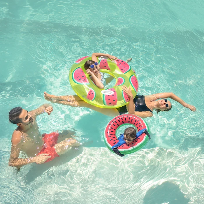 Family relaxing in the pool with watermelon floaties during vacation.