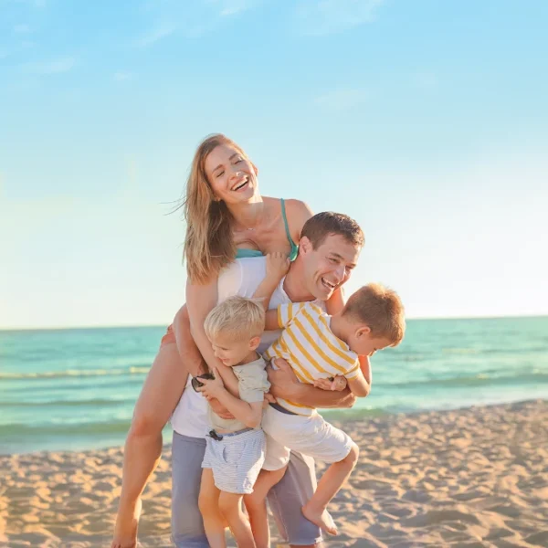 Parents playing and hugging their young children on the beach at sunset.